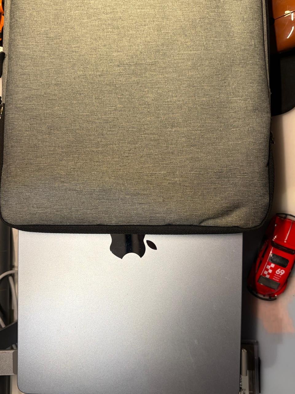 A thin silver laptop being placed into a charcoal backpack on a wooden table.